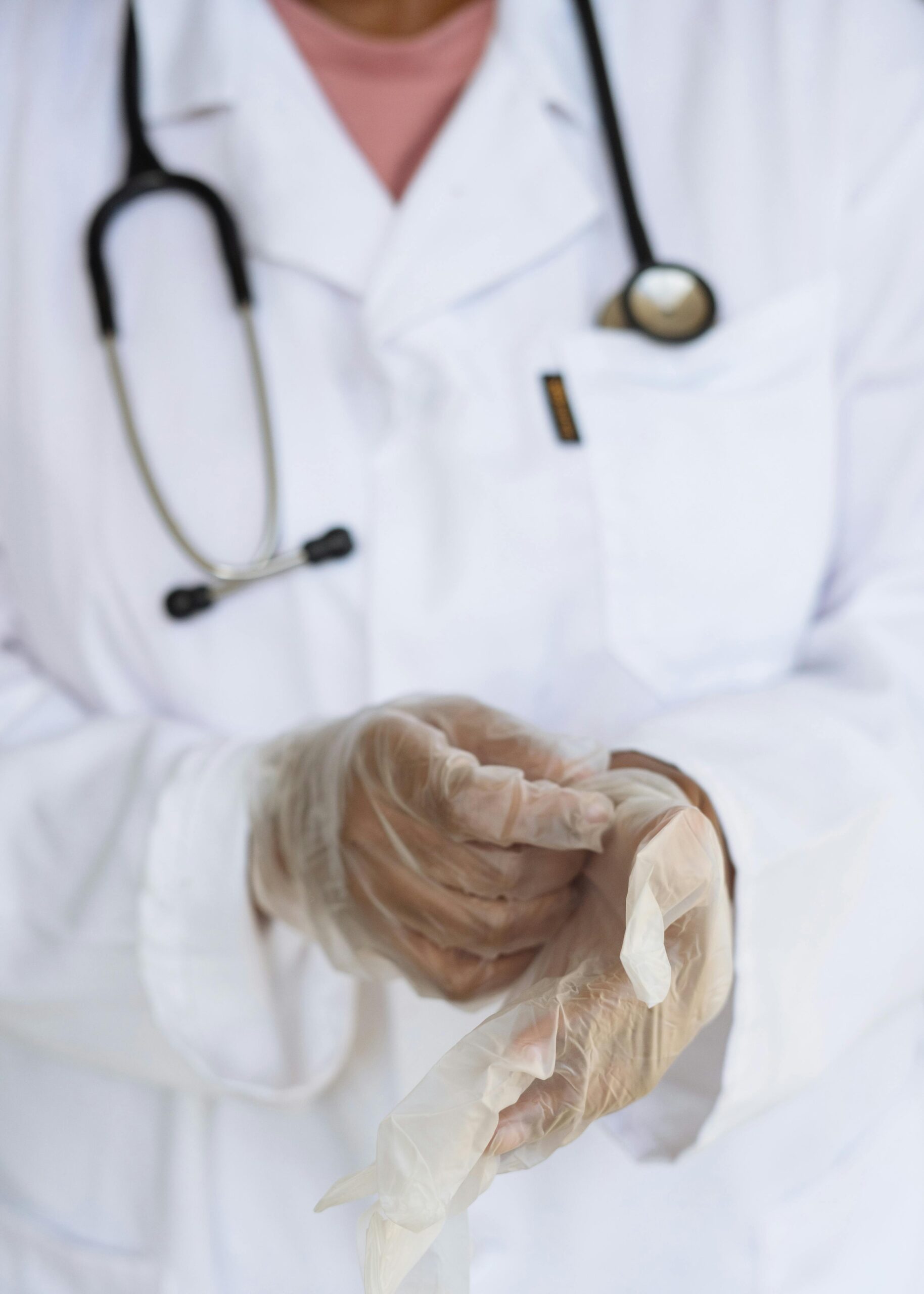 pexels-photo-3825586-3825586 Faceless ethnic medical worker in lab coat and stethoscope taking of transparent gloves after approaching patients for examination in modern hospital